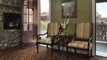 A room with a stone fireplace, two striped chairs, a table with a vase, and a door leading outside.