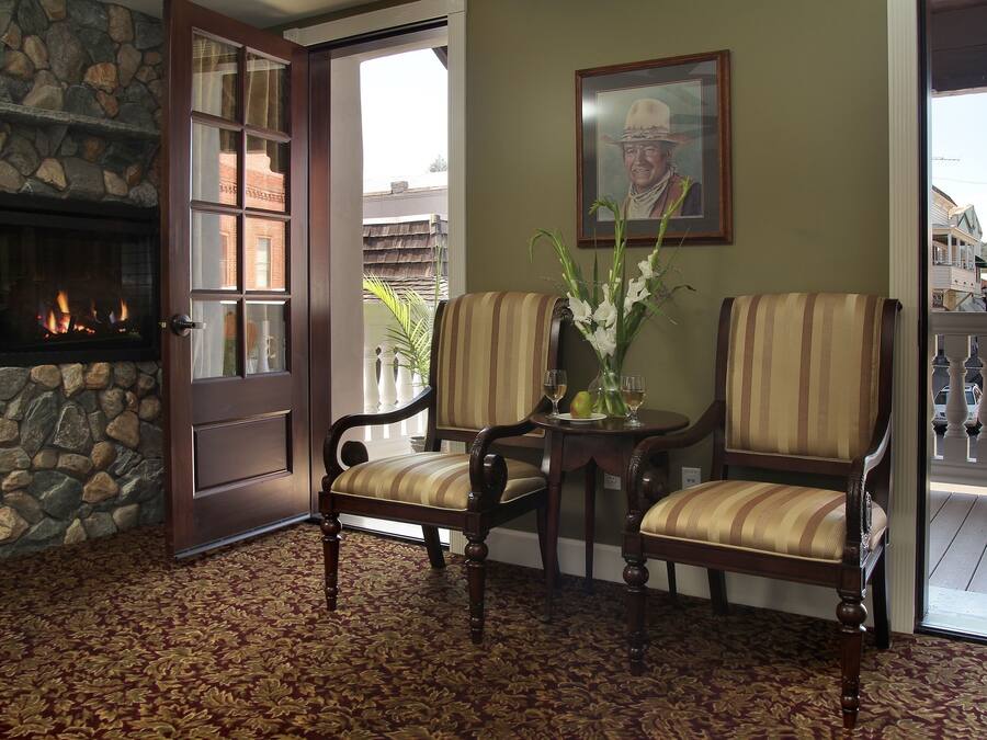 A room with a stone fireplace, two striped chairs, a table with a vase, and a door leading outside.