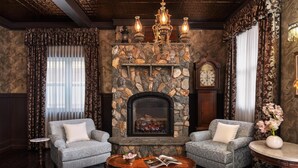 A cozy room with a stone fireplace, two armchairs, a round coffee table, and a clock on the wall. - National Hotel Jackson, Tapestry Collection by Hilton (Jackson)