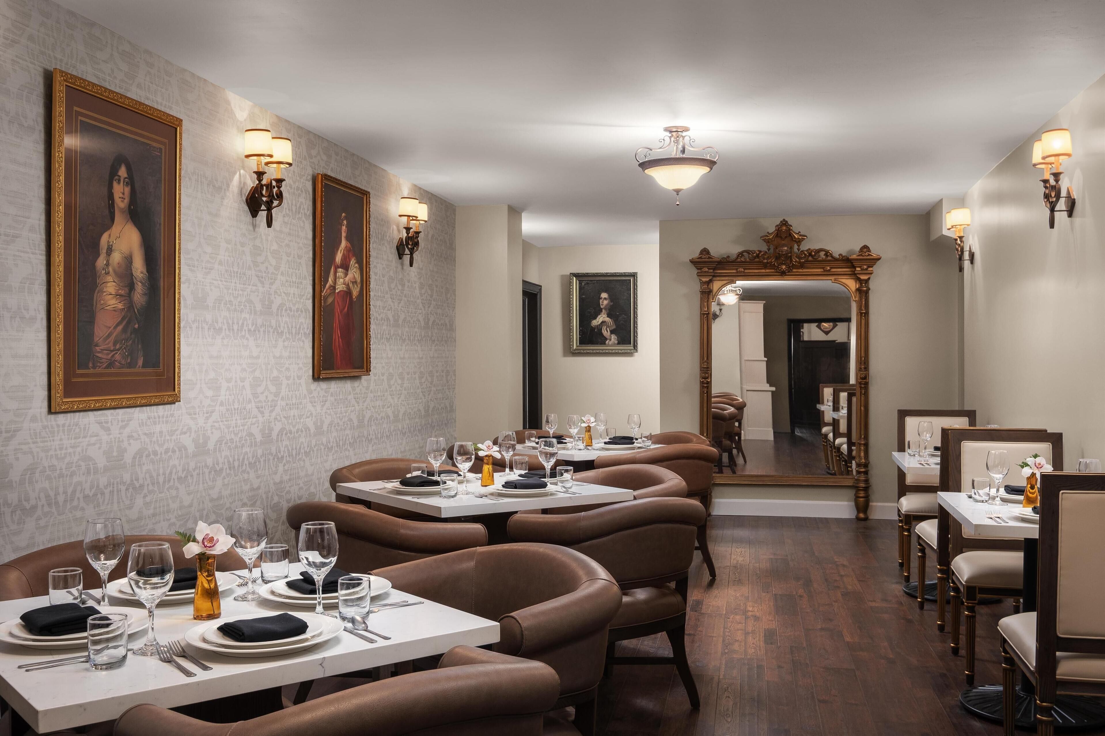 A dining area with tables set for service, framed portraits on the walls, and a mirror reflecting the room.