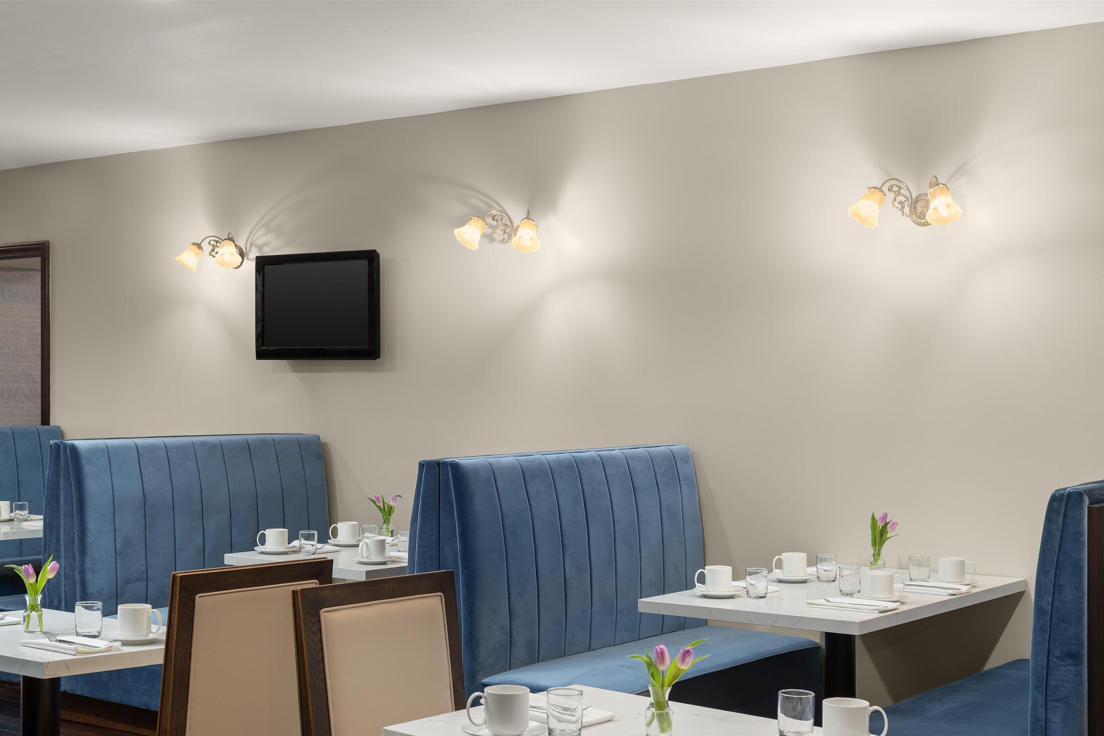 A restaurant with blue booths and white tables, each with a cup, saucer, and glass.