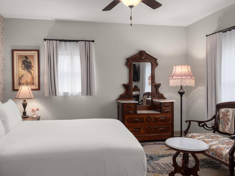 A hotel room with a bed, a dresser, a mirror, a chair, and a ceiling fan.