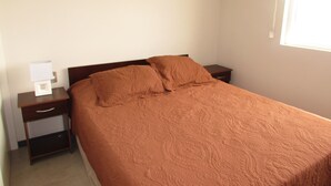 A bedroom with a single bed, a nightstand, a drawer, and a bedside table.
