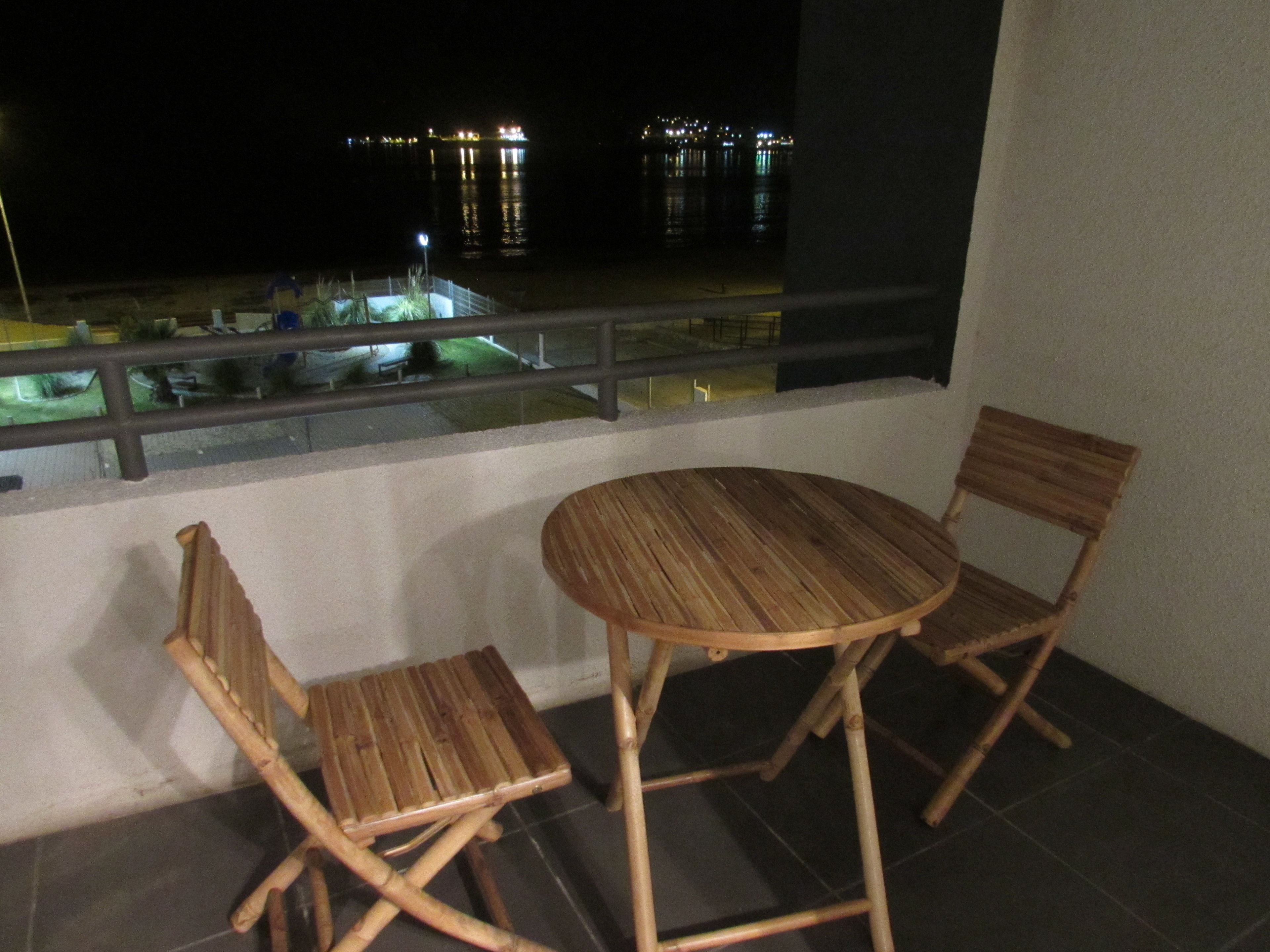 A balcony with a round wooden table and two wooden chairs.