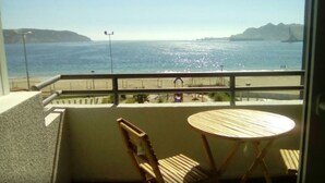 A balcony with a view of the sea, a wooden chair, and a small round table.