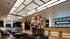 Um hall de hotel moderno com balcão de recepção, área de estar e um arranjo floral grande.