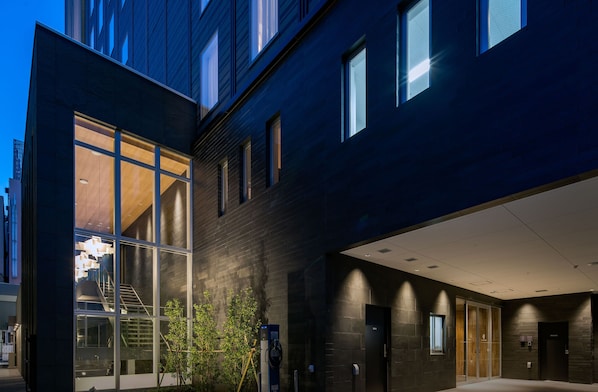 A modern building with large glass windows, a staircase, and a parking area with a charging station.