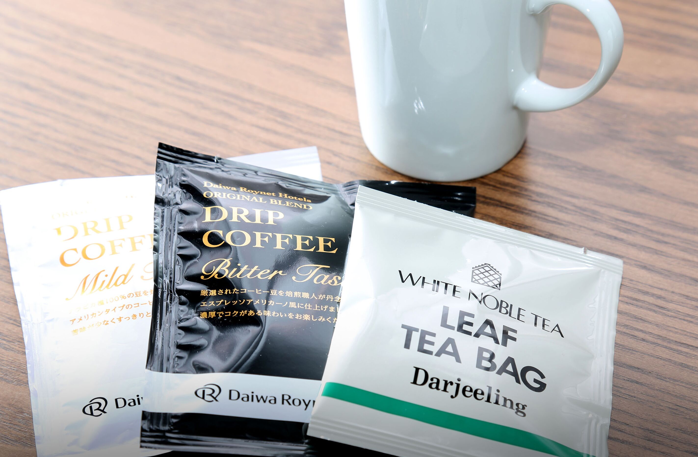 Three tea bags and a white mug on a wooden table.
