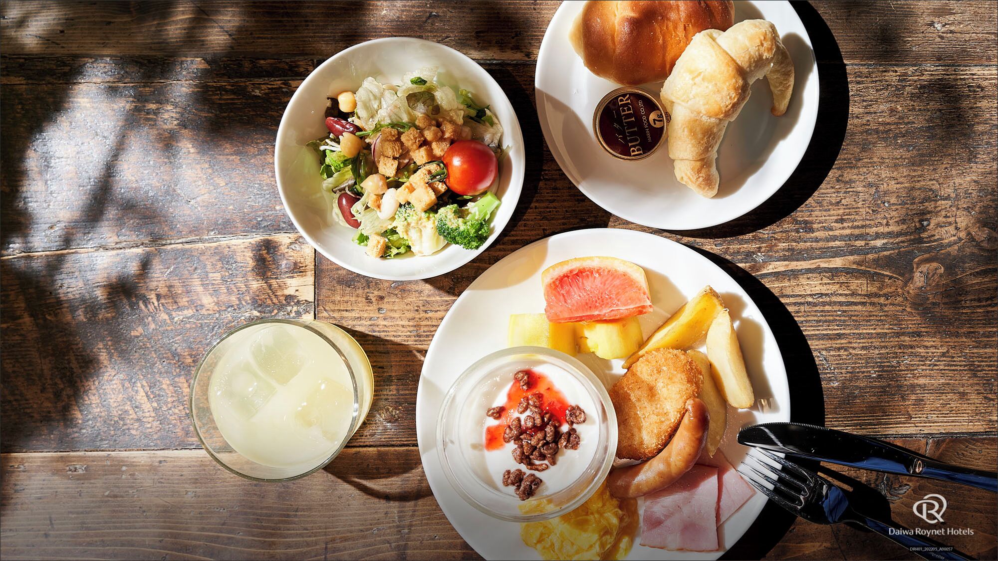 A meal with a salad, bread, fruit, and a drink on a wooden table.
