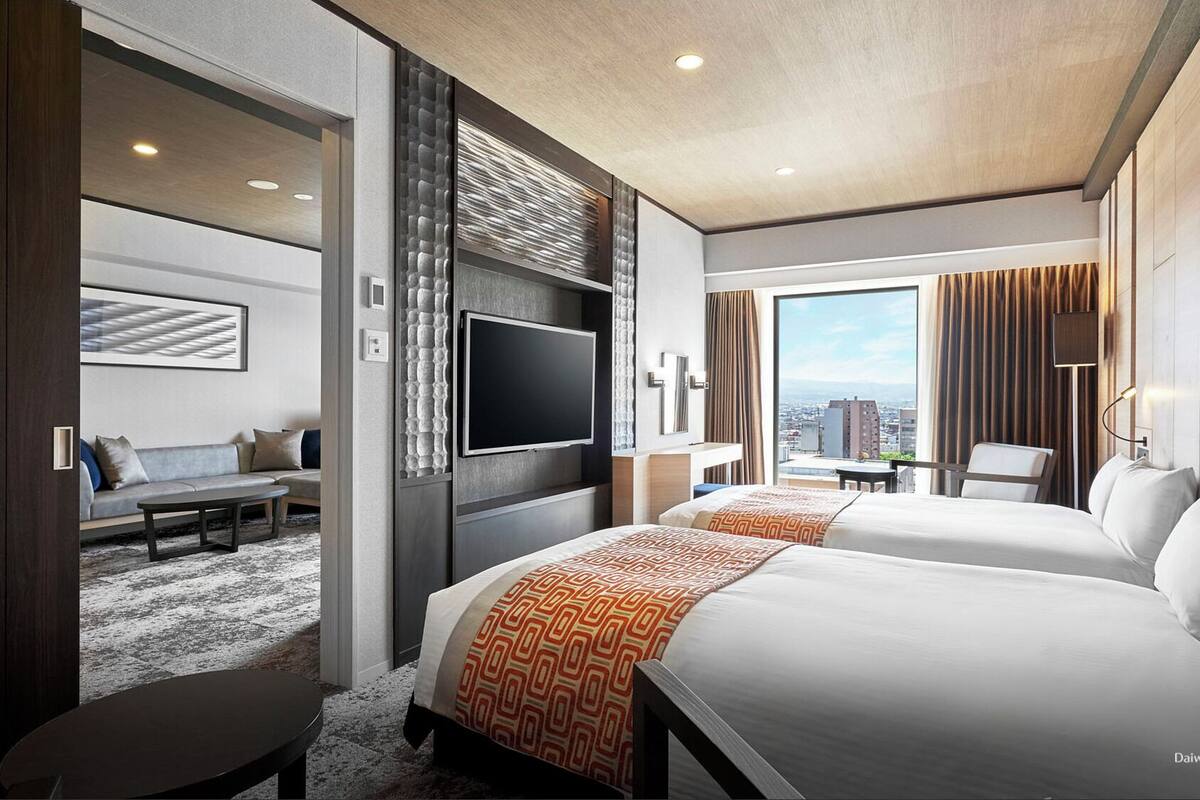 Een hotelkamer met twee bedden, een televisie, een bureau en uitzicht op de stad.