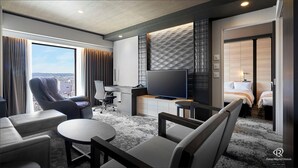 Quarto de hotel moderno com uma janela grande, televisão de tela plana, escrivaninha e uma cama.