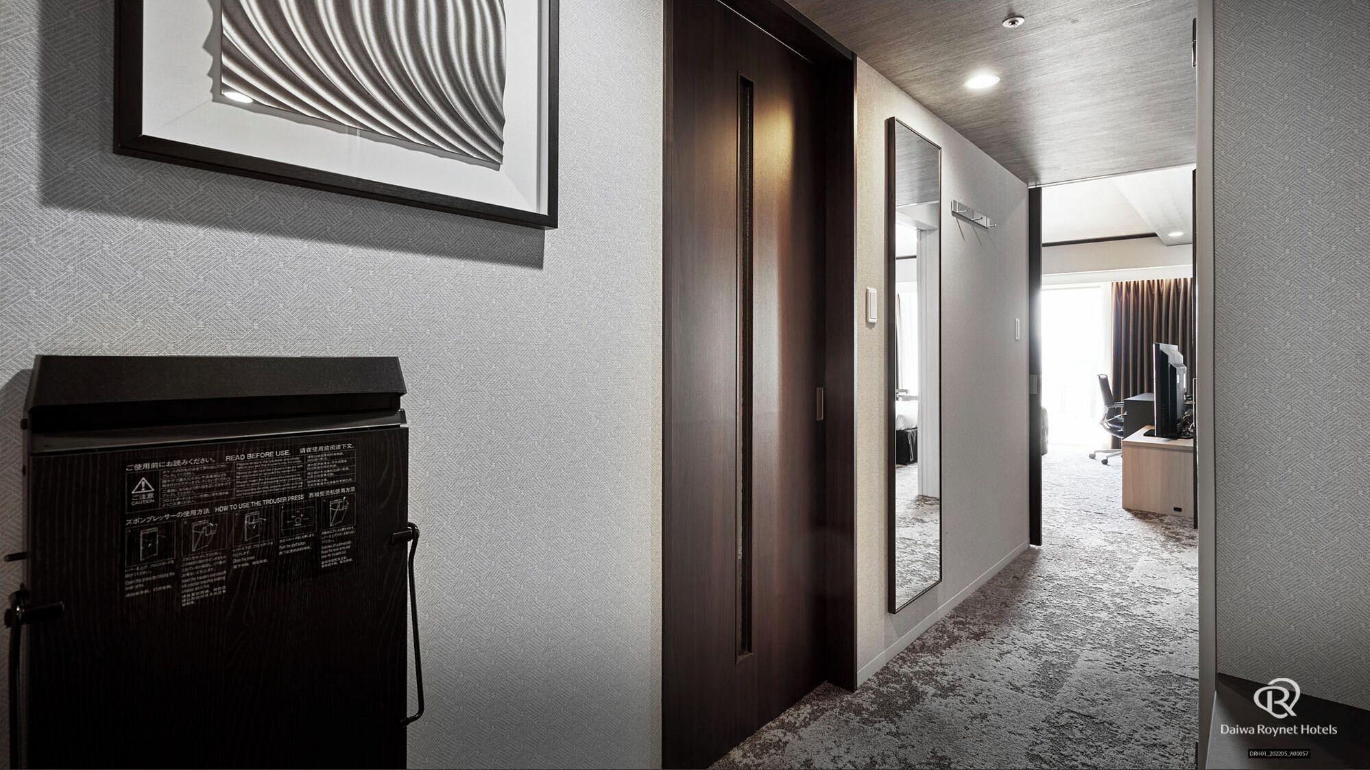 Un couloir d’hôtel avec une porte en bois sombre, une œuvre d’art encadrée au mur et un sol recouvert de moquette.