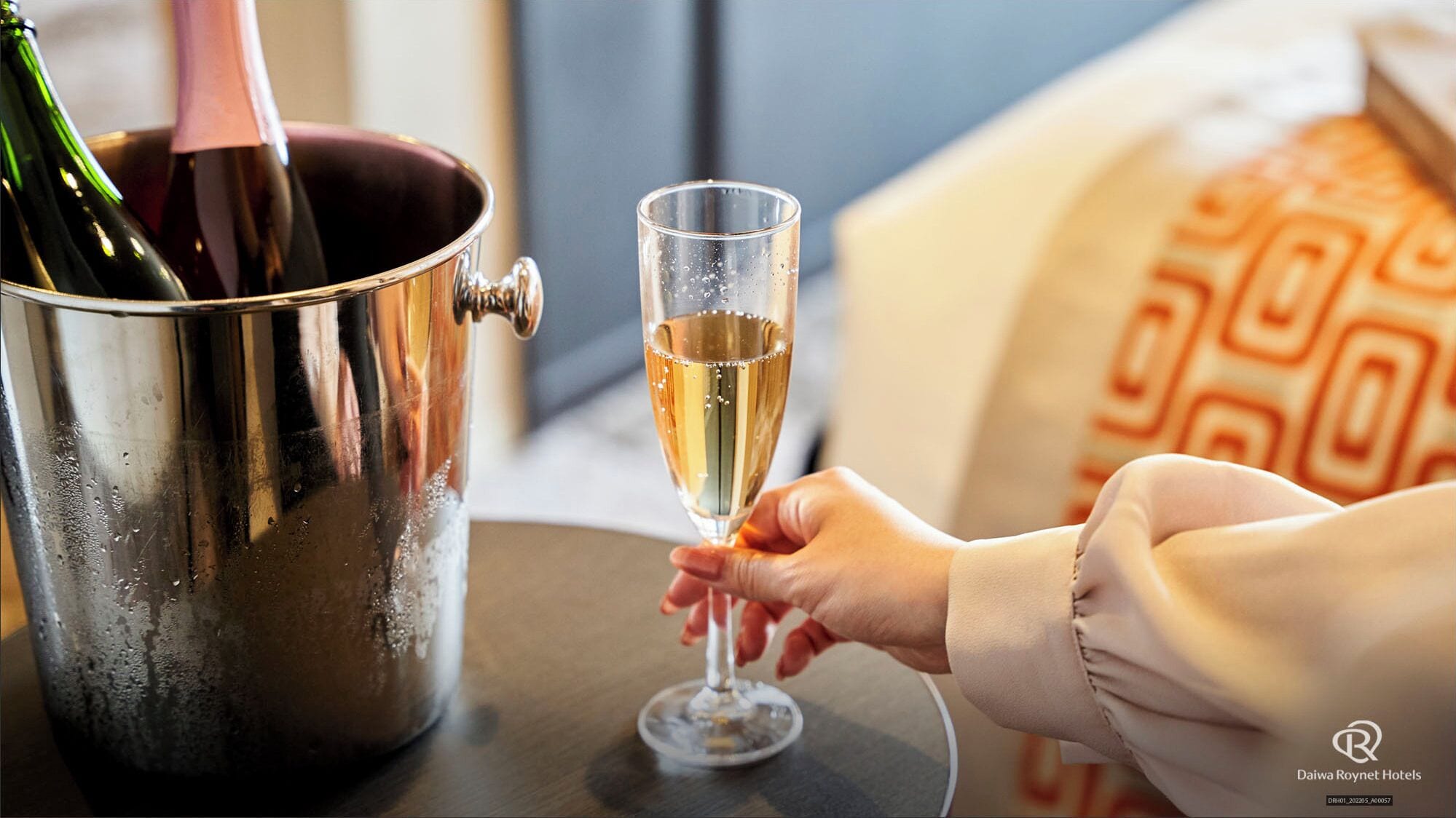 A hand holding a champagne flute next to a champagne bucket.