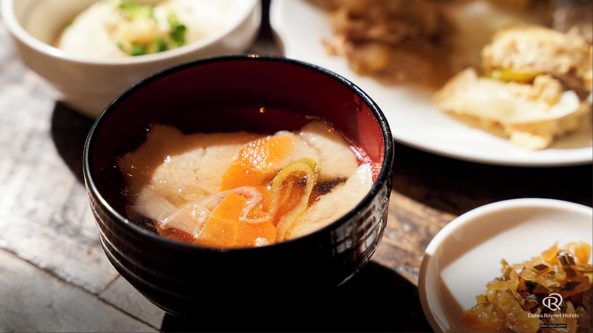 Un tazón de sopa con caldo transparente y rodajas de naranja, servido en un tazón negro.