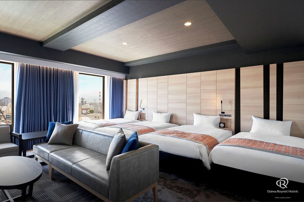 Een hotelkamer met een bank, twee bedden, een eettafel en uitzicht over de stad.