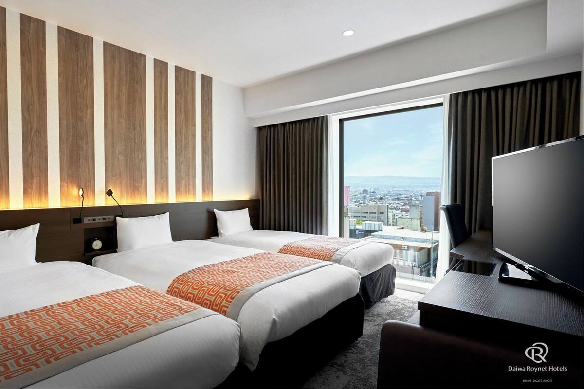 Een hotelkamer met twee bedden, een televisie en uitzicht over de stad.