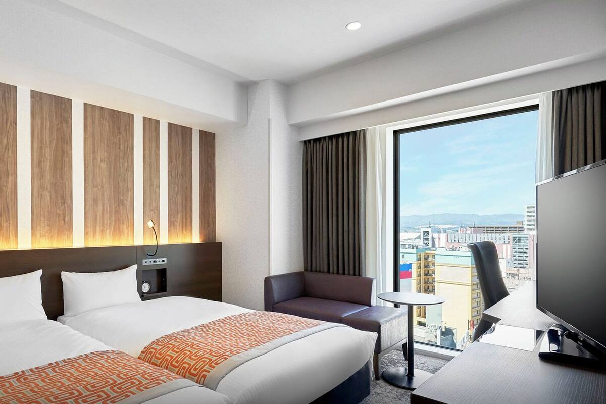 Een hotelkamer met een groot bed, een bureau, een stoel en een televisie. Er is uitzicht op de stad vanuit het raam.