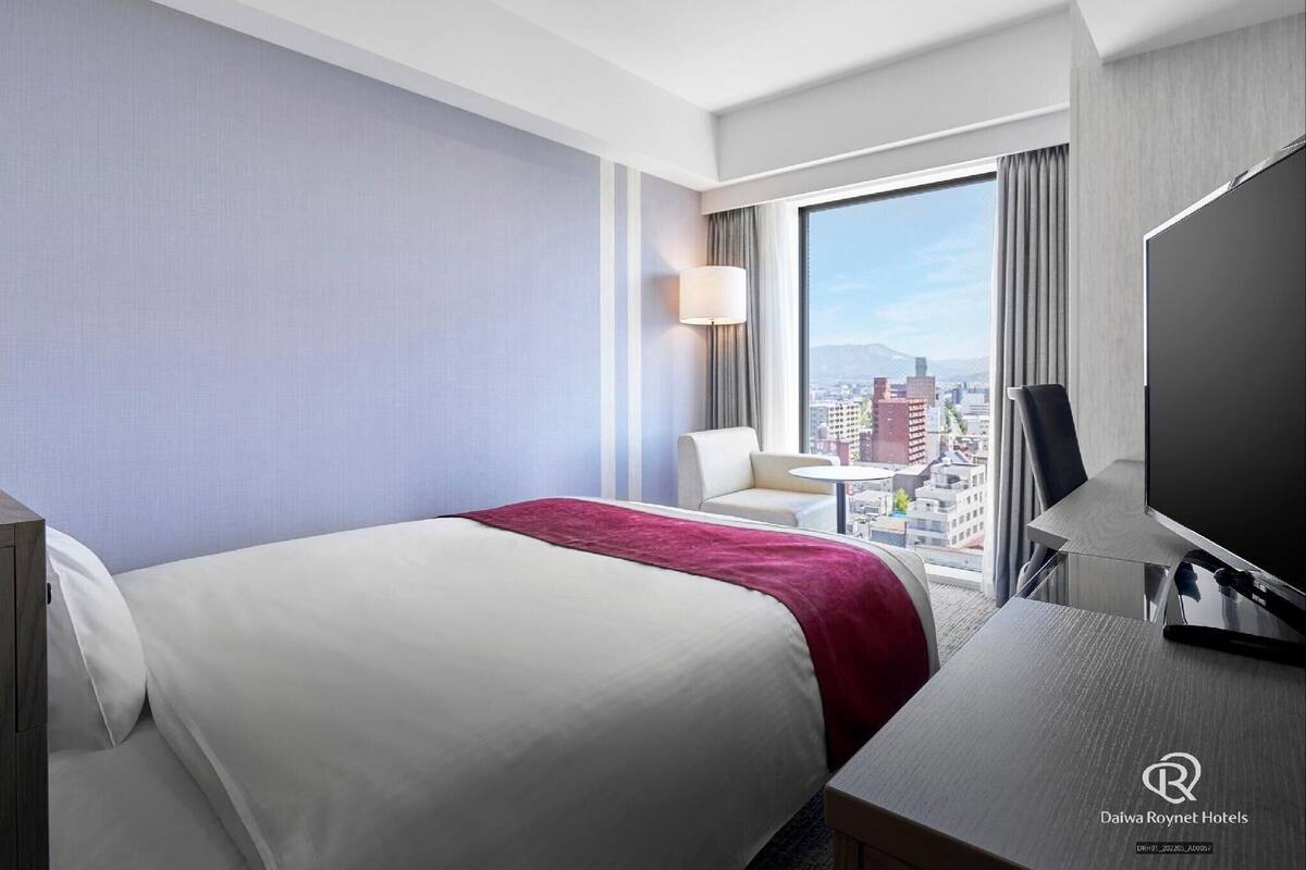Een hotelkamer met een bed, een bureau, een stoel, een televisie en uitzicht op de stad.