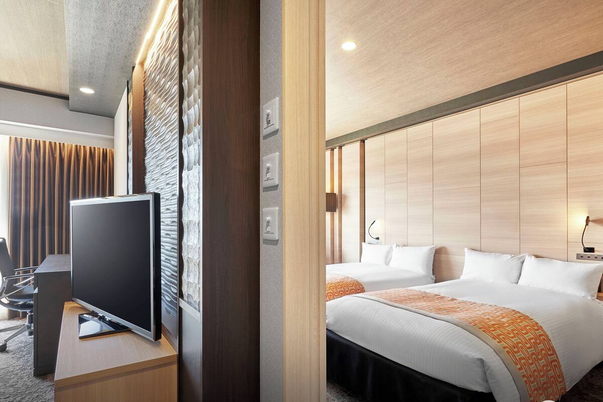 Hotelkamer met een flatscreen-tv, een bed met witte beddengoed en een oranje plaid, en een houten hoofdbord.