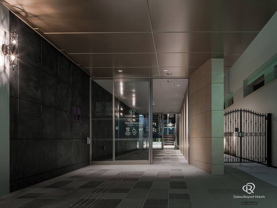 A modern hotel corridor with glass doors, a metal gate, and a tiled floor.