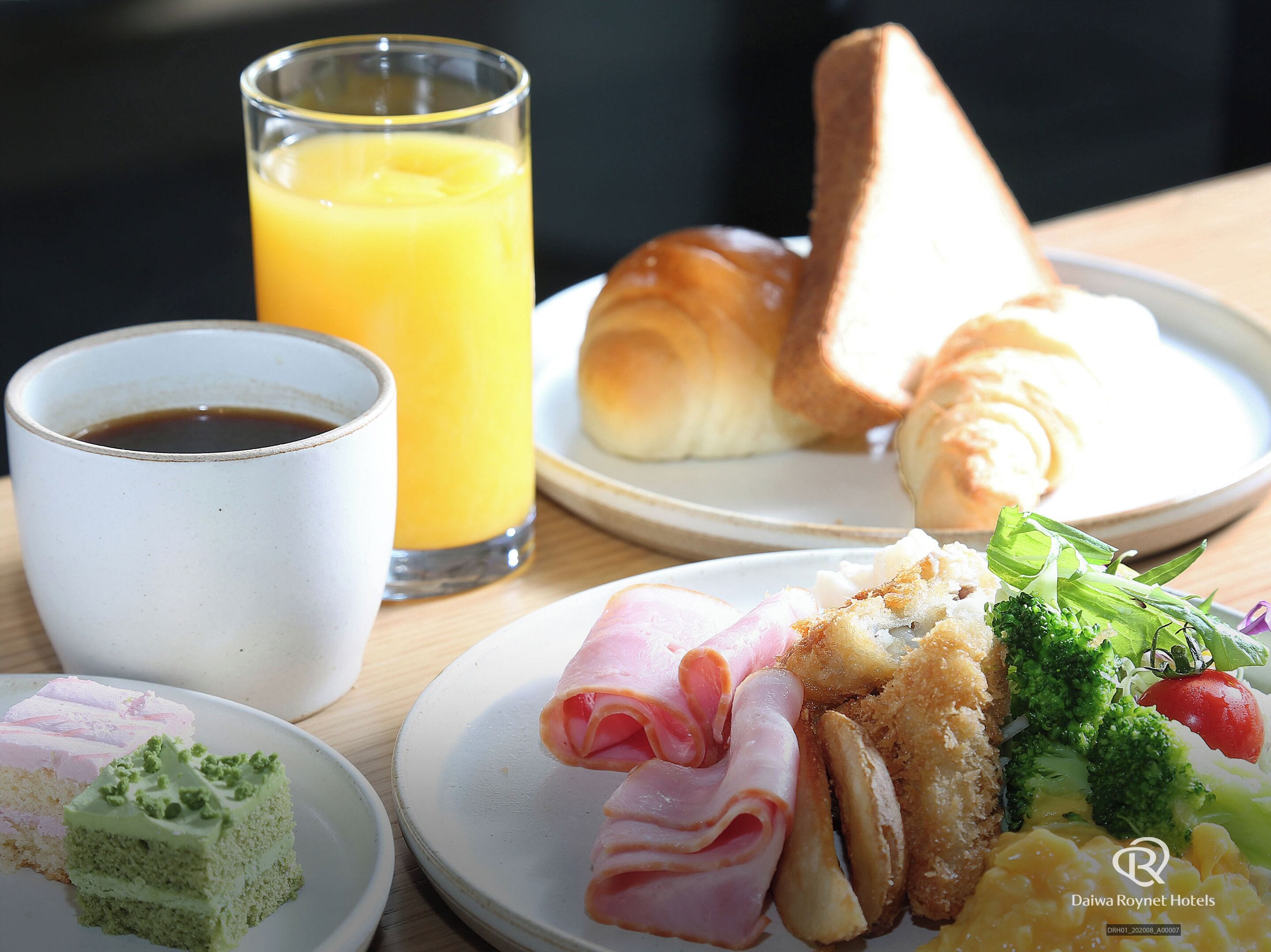 A breakfast plate with ham, croissant, and vegetables, a glass of orange juice, and a cup of coffee.