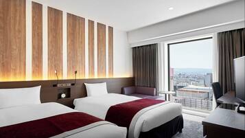 Hotelkamer met twee bedden, een bureau, een stoel en een groot raam met uitzicht op de stad.