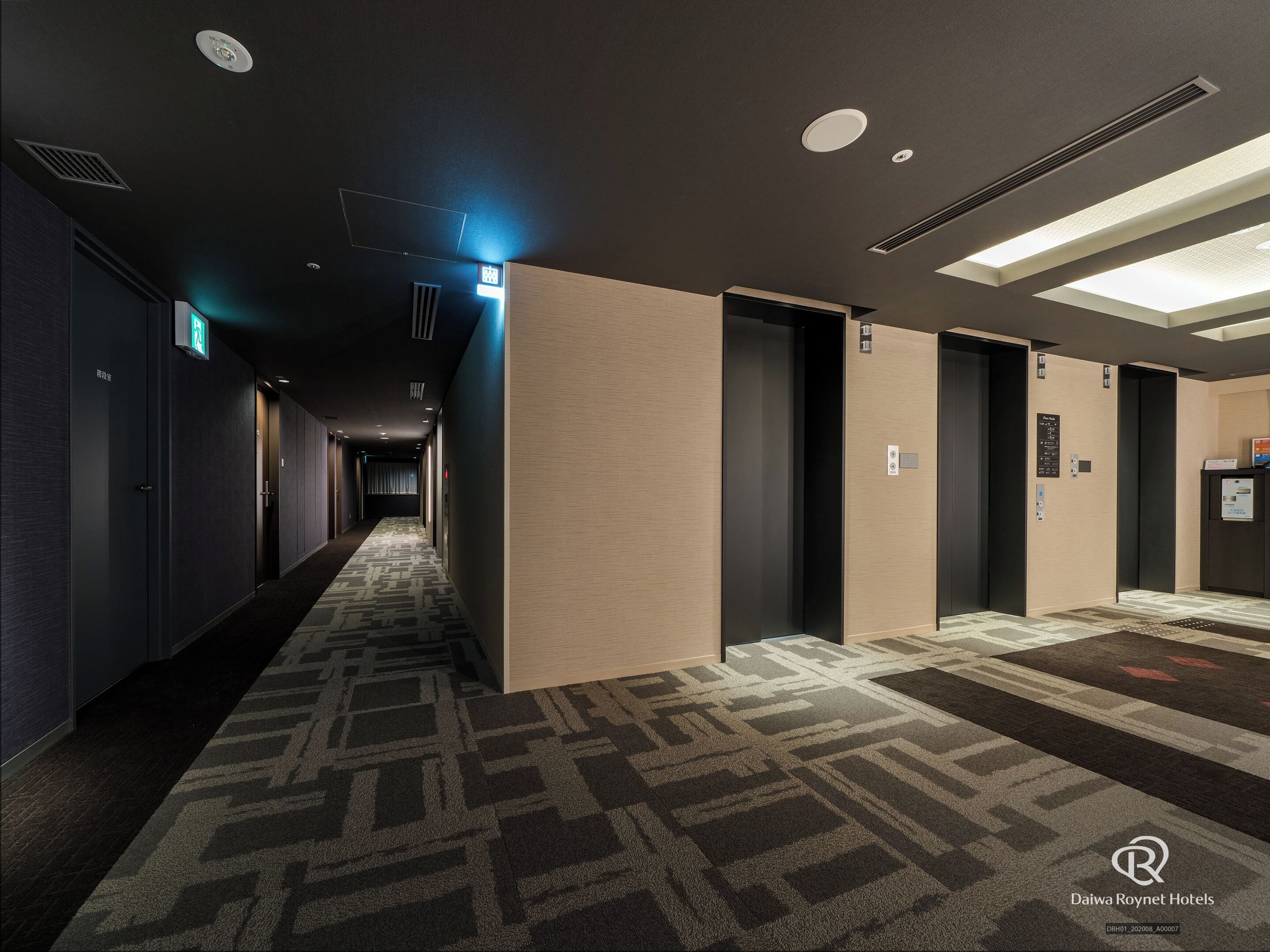 A hotel corridor with carpeted flooring, recessed lighting, and doors leading to rooms.