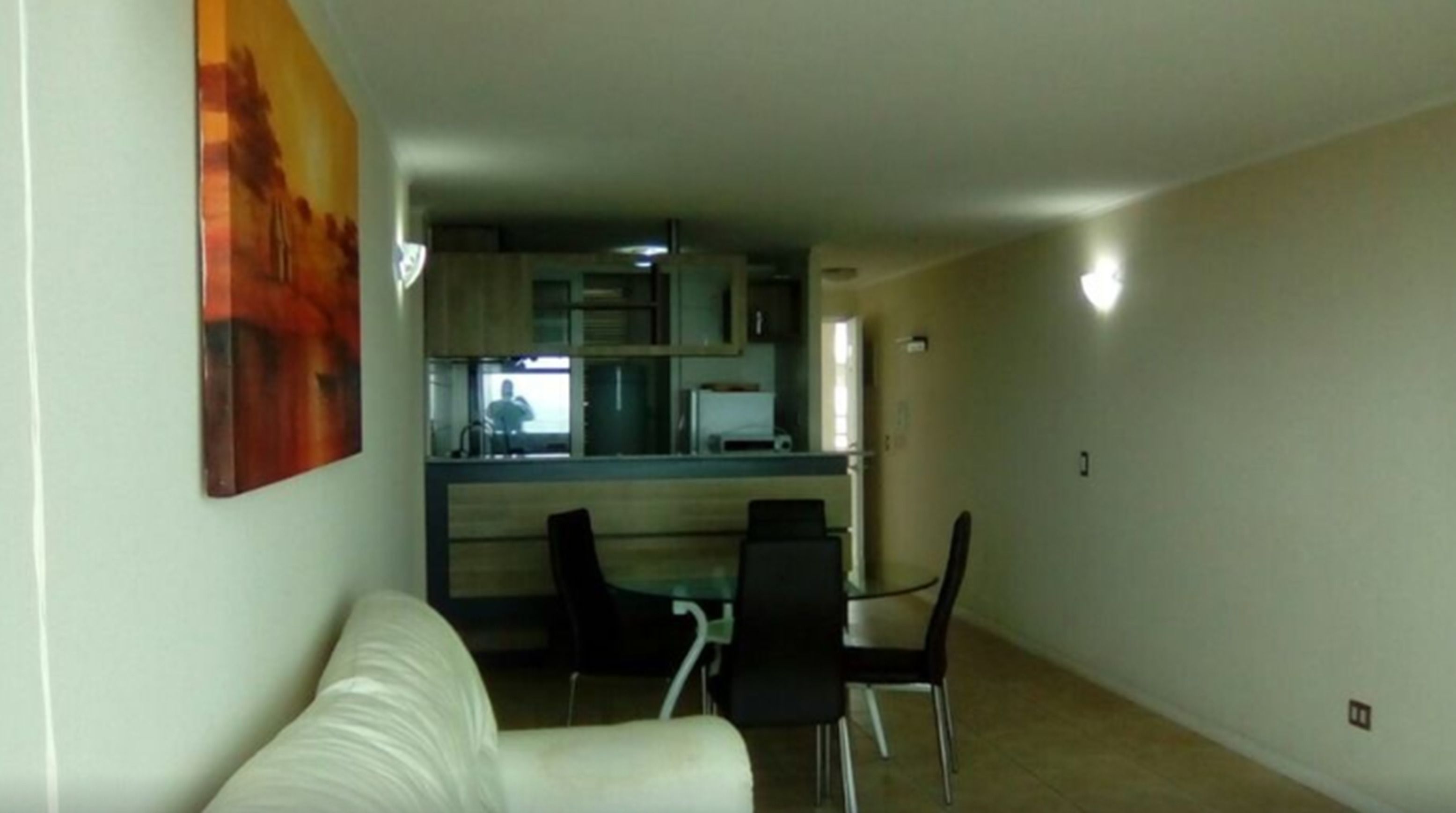 A living room with a white sofa, a dining area with two black chairs, and a kitchen in the background.
