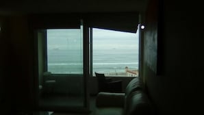 A room with a large window overlooking a beach, a sofa, and a small table. - 47.- HNA Mirador El Faro (La Serena)