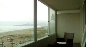 Una habitación con un ventanal grande que ofrece vistas a una playa y montañas distantes.