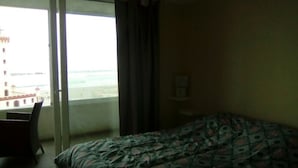 A hotel room with a bed, a chair, and a view of the sea and buildings. - 47.- HNA Mirador El Faro (La Serena)