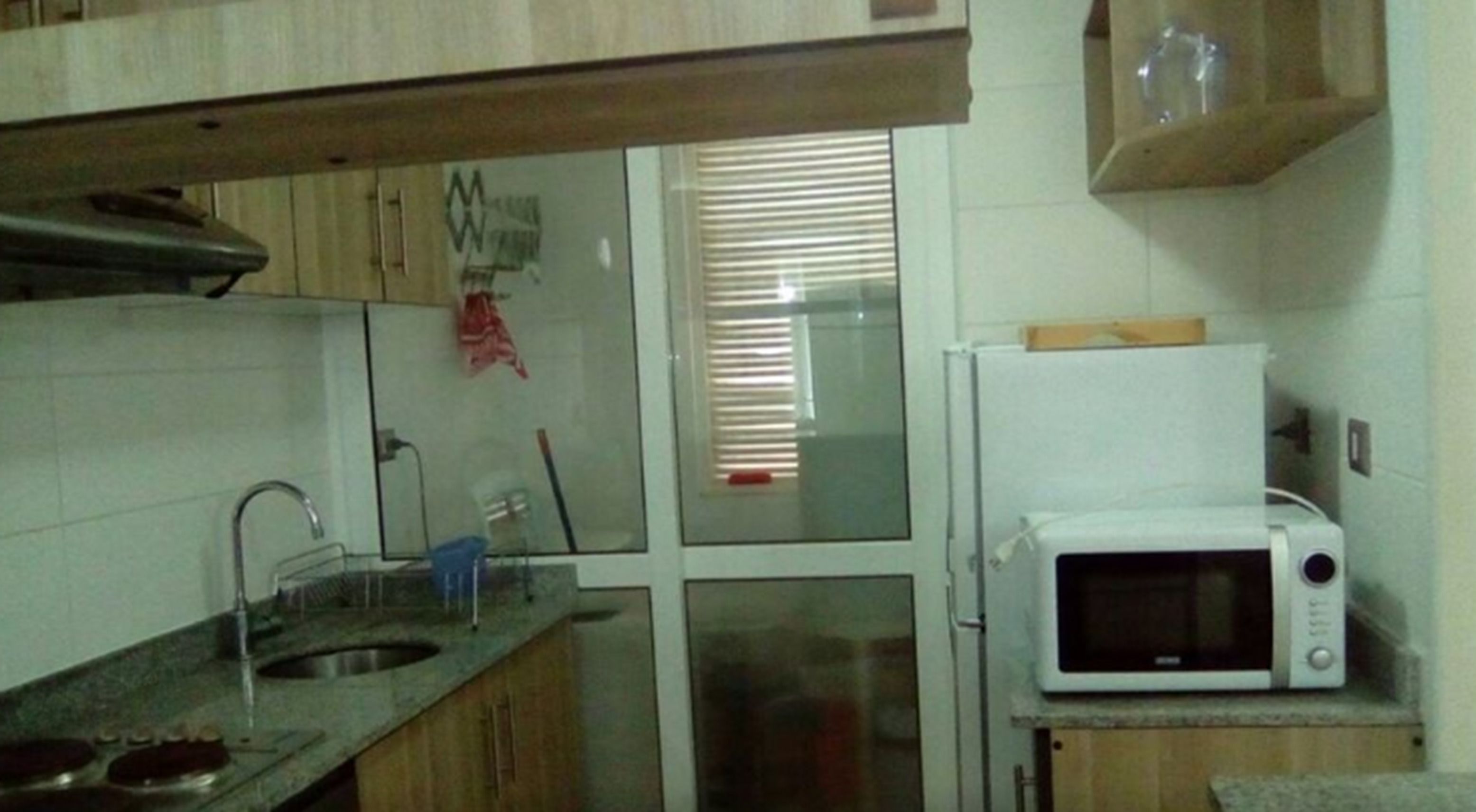 A small kitchen with a sink, a microwave, and a window with blinds.