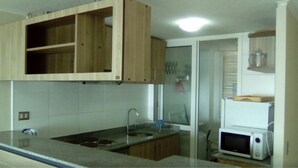 A kitchen with wooden cabinets, a sink, a microwave, and a glass door leading to another room. - 47.- HNA Mirador El Faro (La Serena)