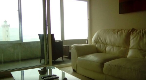 Un salón con un ventanal grande, un sofá de cuero, una mesa de centro de cristal y una silla.