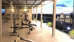 Un gimnasio al aire libre con diverso equipo de ejercicios, incluyendo una prensa de banca, mancuernas y un soporte para pesas.
