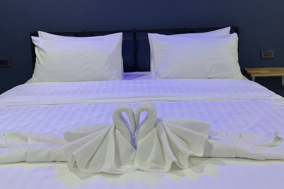 A neatly made bed with white linens and a towel arranged in a heart shape at the foot of the bed.
