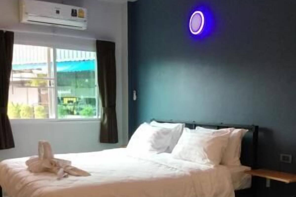 A hotel room with two beds, a window with curtains, an air conditioning unit, and a wall-mounted light.