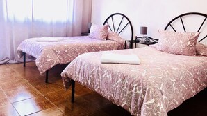 A room with two beds, each with a patterned bedspread and pillows, a small table with a lamp, and a window with sheer curtains. - Suites do Pinhal (Proenca-a-Nova)