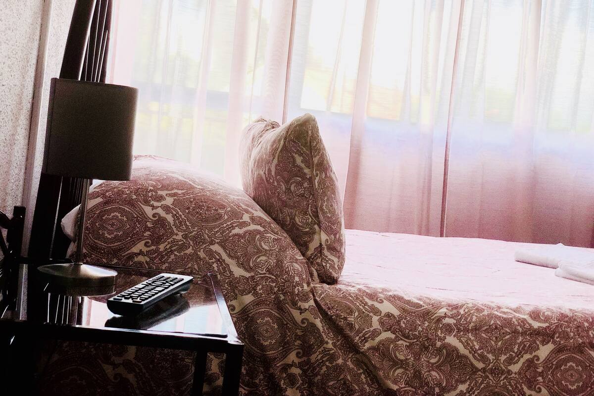 A hotel room with a bed, a nightstand, a lamp, and a remote control.