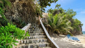 Una escalera de piedra que conduce a una playa con palmeras y una vista despejada del océano.
