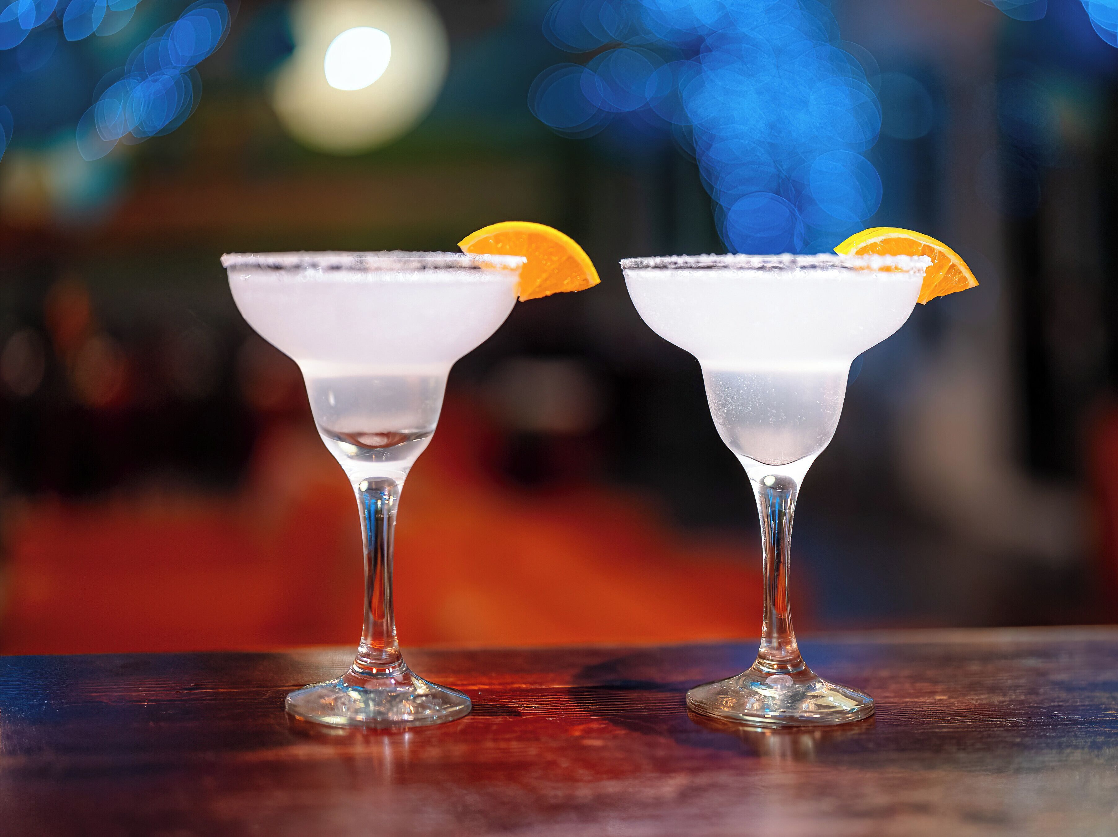 Deux verres à martini contenant un liquide clair et décorés d’une tranche d’orange, posés sur une surface en bois.