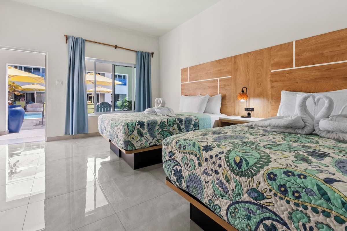 A hotel room with two beds, a wooden headboard, a nightstand, and a view of the outdoor area with umbrellas.