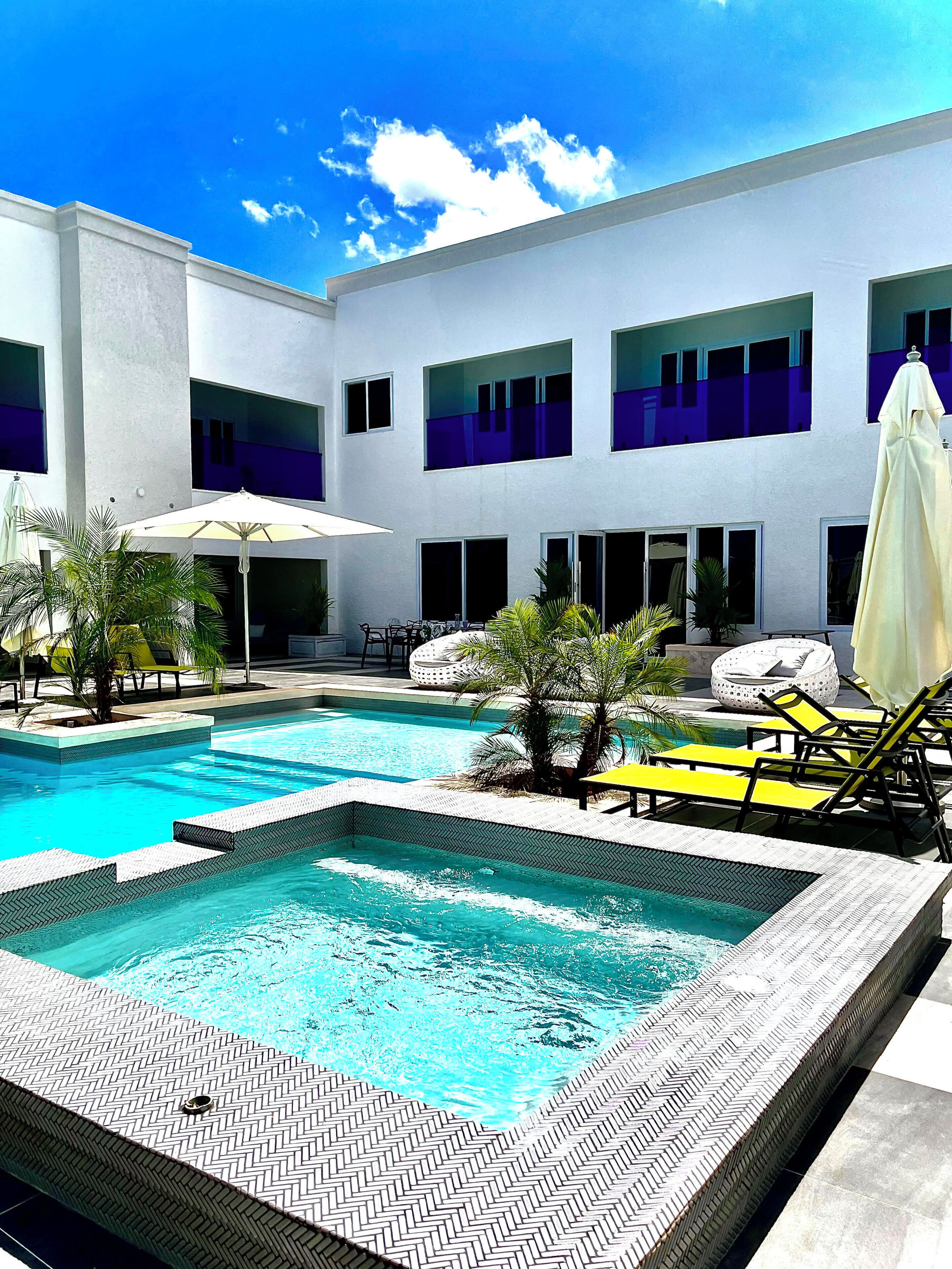 A swimming pool area with lounge chairs and umbrellas, surrounded by a building with multiple windows and balconies.