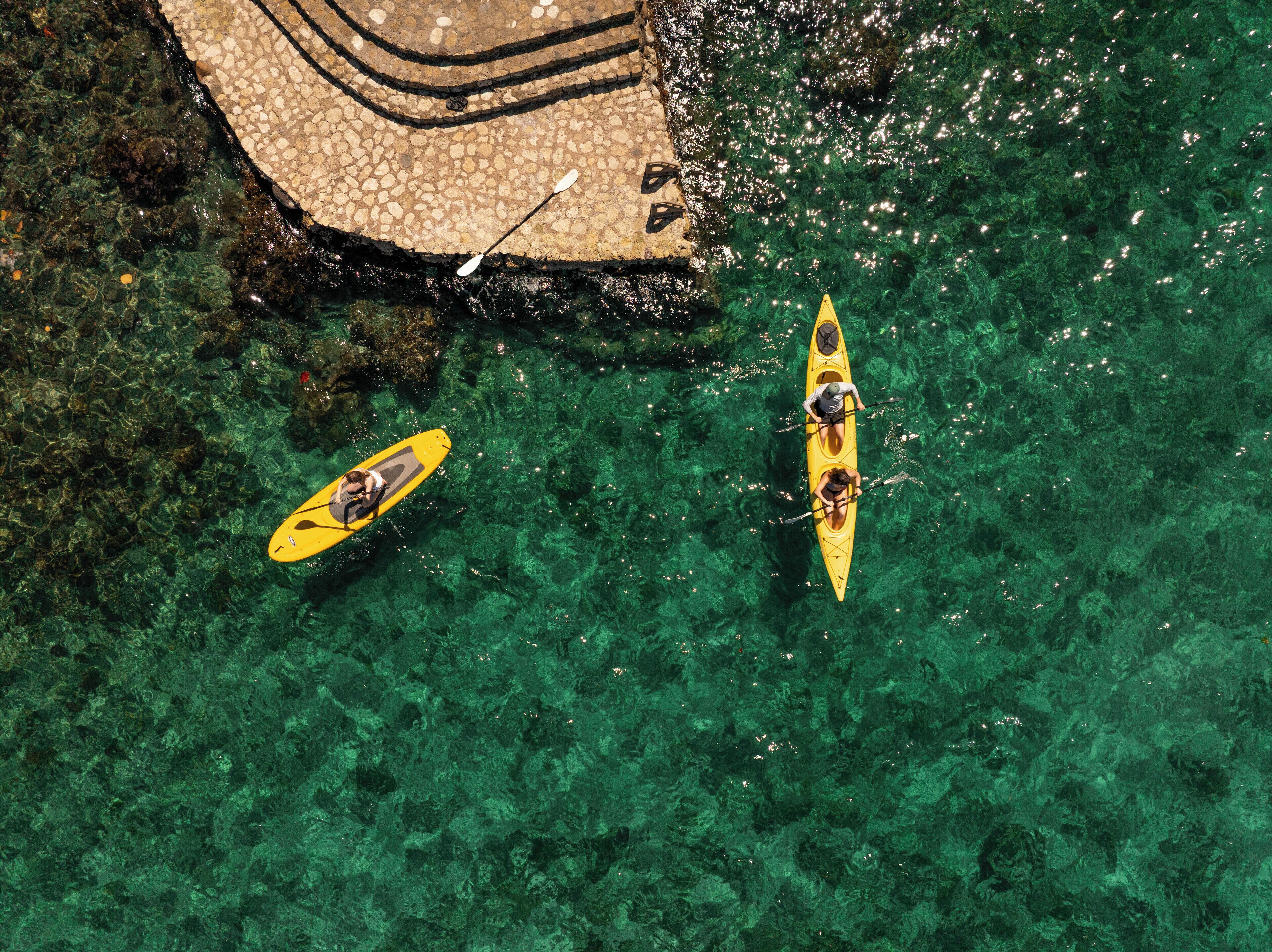 Dos kayaks en una masa de agua cristalina con un sendero de piedra cercano.