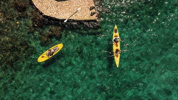 Two kayaks on a clear water body with a stone pathway nearby.