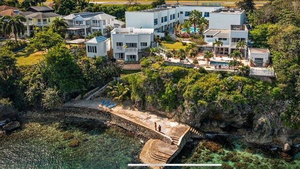 Un hotel costero con varias edificaciones, una piscina y un litoral rocoso.