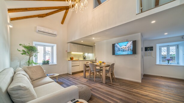 A spacious living area with a high ceiling, wooden beams, a dining table, and a TV mounted on the wall. - Feel like an Emperor Apartment (Split)