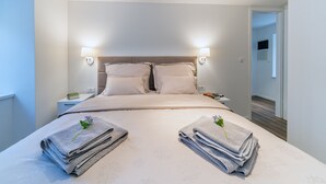 A neatly made bed with two pillows, a bedside table with a lamp, and two folded towels with a flower on each. - Feel like an Emperor Apartment (Split)