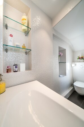 A bathroom with a white bathtub, glass shelves with toiletries, and a white toilet. - Feel like an Emperor Apartment (Split)