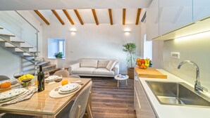 A modern kitchen with a dining area, wooden beams on the ceiling, a built-in sink, and a staircase leading to a loft bedroom. - Feel like an Emperor Apartment (Split)